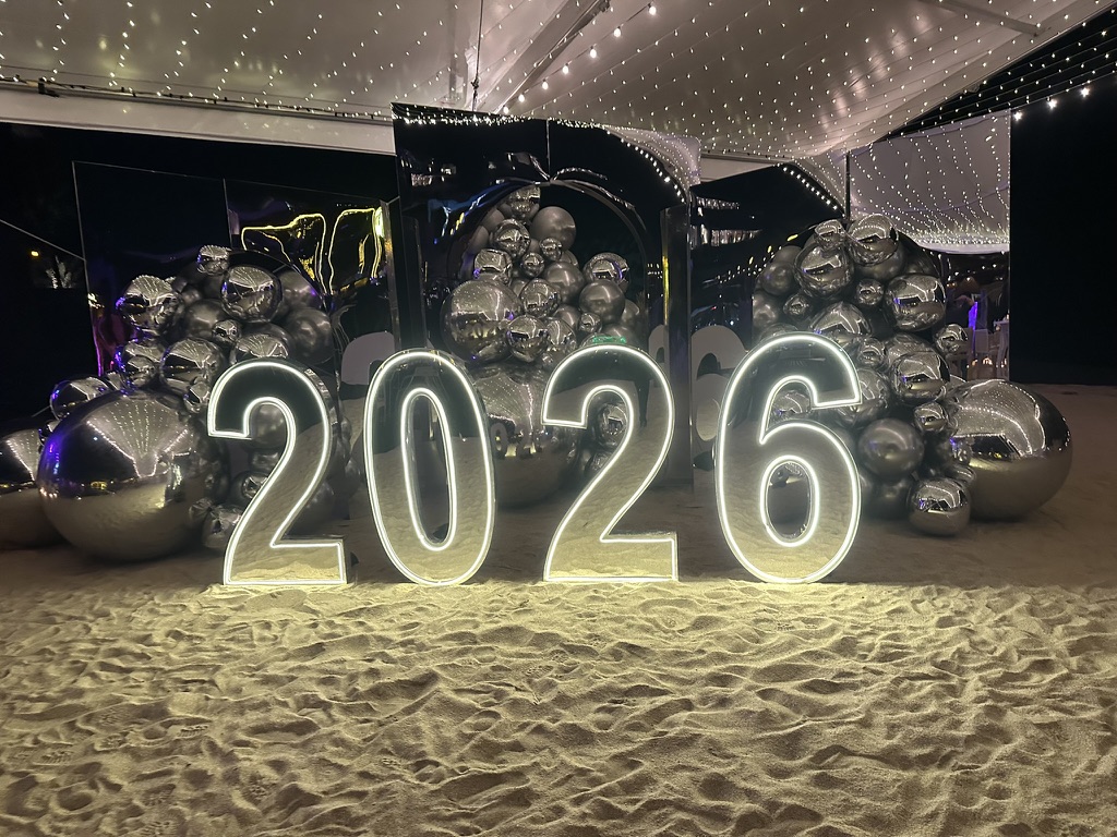 Illuminated 2026 numbers with silver balloon installation on beach sand NYE decor