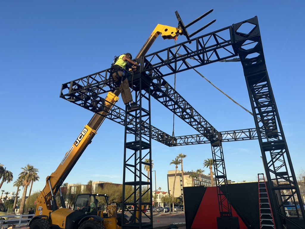 Rigger at height on steel truss structure JCB telehandler event activation build Phoenix AZ