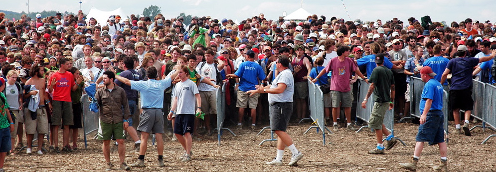 Safety team in blue shirts directing audience crowd flow behind barricade line festival operations