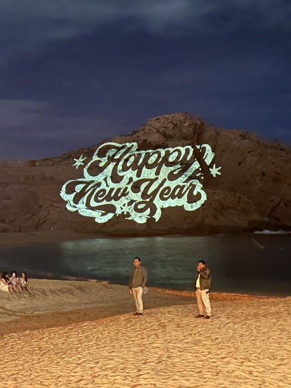 Happy New Year gobo projection onto cliff face over beach — destination event production Cabo San Lucas